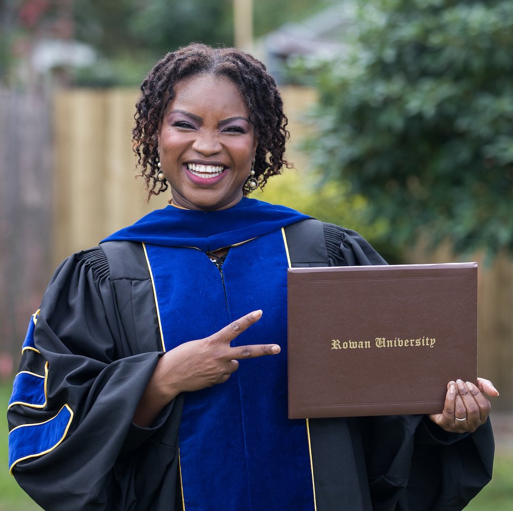 New doctoral graduate beams while holding her new diploma and wearing academic regalia.