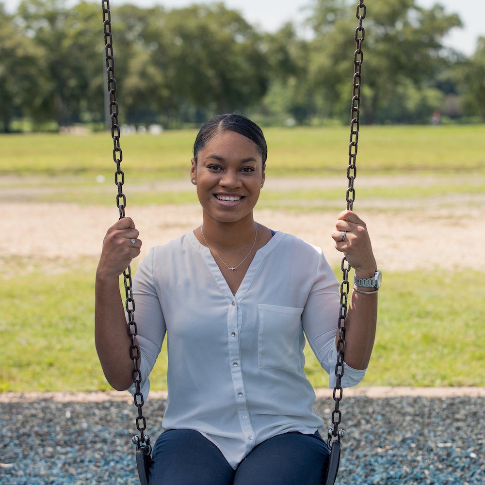Alisha sits on a swing at a park, holding on to the chains.