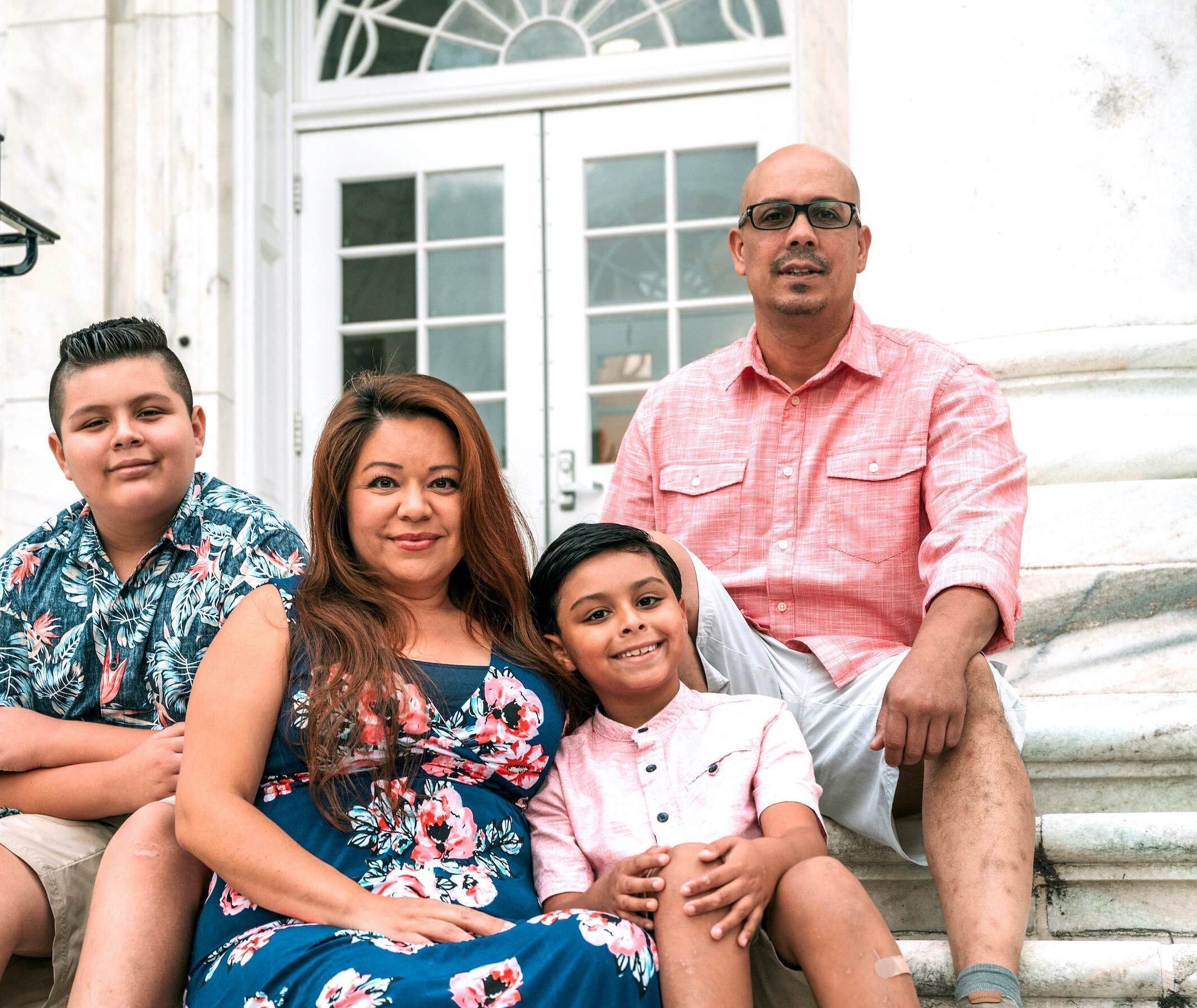 A mom and dad sit with their two sons on marble steps.