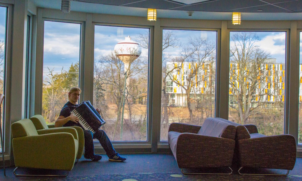 A male student plays accordion with Rowan water tower in background.