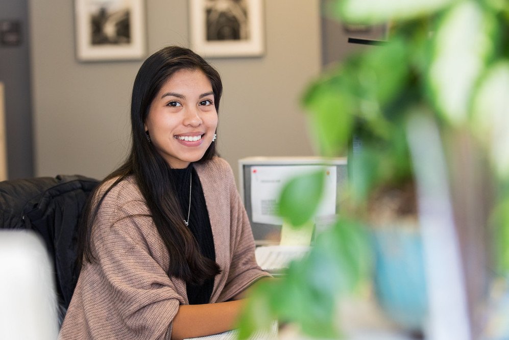 Student works online at her desk, adorned with plants. 